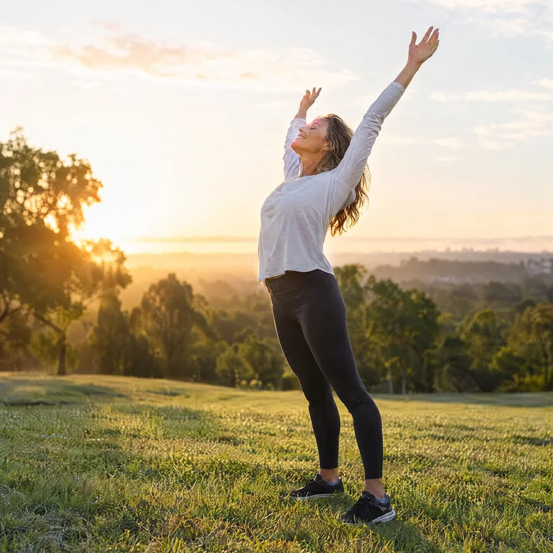 Mujer estirándose con los brazos en alto en un parque al amanecer